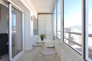 A balcony with a sliding glass door, a small round table with a potted plant, and white chairs. - Charming apartment for rent in Roses, Costa Brava! 0 meters from the beach. Enjoy the community pool and sea views. (Roses)