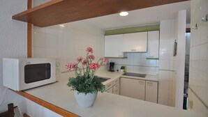 Een keuken met witte kastjes, een magnetron, een spoelbak en een bloempot met roze bloemen.