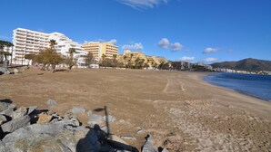 Een strand met een rotsachtig voorgronddeel, een zandstrand en een rij meerverdiepingen tellende hotelgebouwen op de achtergrond.