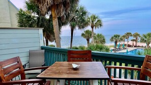 Une terrasse en bois avec une table et des chaises, donnant sur une plage et une piscine.