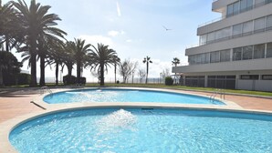Ein Pool mit geschwungener Form, umgeben von Palmen und einem modernen Gebäude mit großen Fenstern.