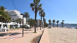 Eine Strandpromenade mit Palmen, einem Sandstrand und einem mehrstöckigen weißen Gebäude.