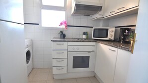 A compact kitchen with white cabinets, a microwave, a built-in oven, and a washing machine. - Apartment in Costa Brava, 2 bedrooms for 6 people, mountain views, community pool, close to beach, supermarket and restaurants. (Roses)