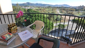 A balcony with a view of a valley and mountains, a table with drinks and snacks, and a chair. - Apartment in Costa Brava, 2 bedrooms for 6 people, mountain views, community pool, close to beach, supermarket and restaurants. (Roses)
