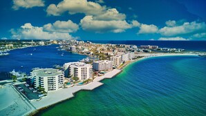 Vue aérienne d’une ville côtière avec un port de plaisance, des hôtels en bord de mer et un ciel bleu dégagé.