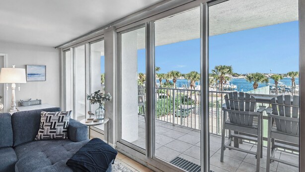 Un salon moderne doté d’une grande porte-fenêtre coulissante donnant sur un balcon avec vue sur une marina et des palmiers.