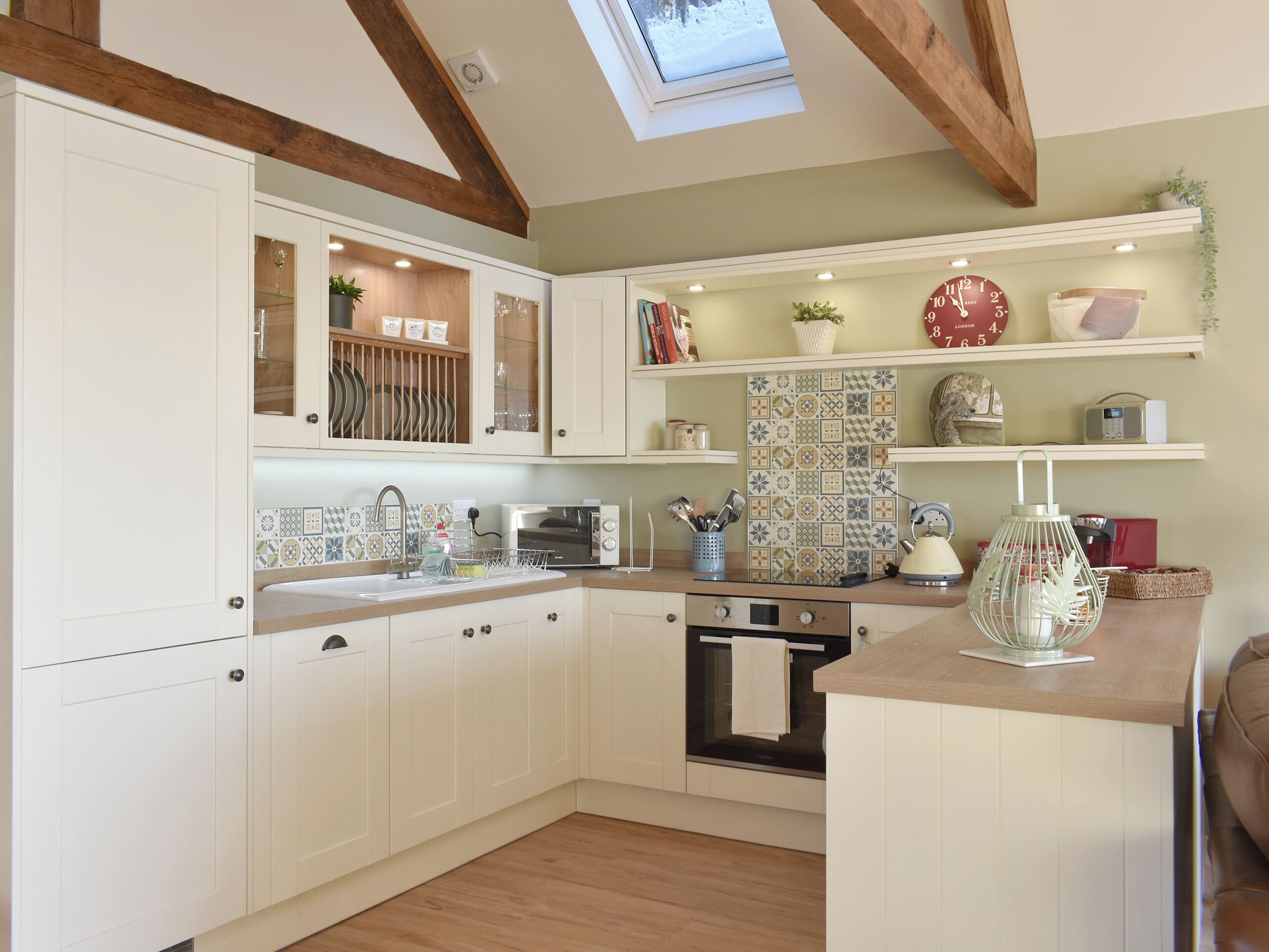A modern kitchen with white cabinetry, a skylight, and a variety of decorative items on the shelves.