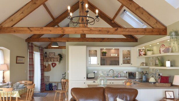 A spacious living area with a high ceiling, wooden beams, a brown leather sofa, and a dining area with wooden chairs and a table. - 2 bedroom accommodation in Sedgefield (Sedgefield)