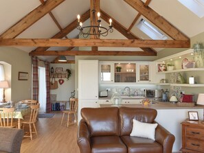 A spacious living area with a high ceiling, wooden beams, a brown leather sofa, and a dining area with wooden chairs and a table. - 2 bedroom accommodation in Sedgefield (Sedgefield)