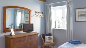 A bedroom with a wooden dresser, a television, a chair with a cushion, a window with curtains, and a bed with a blue blanket. - 2 bedroom accommodation in Sedgefield (Sedgefield)