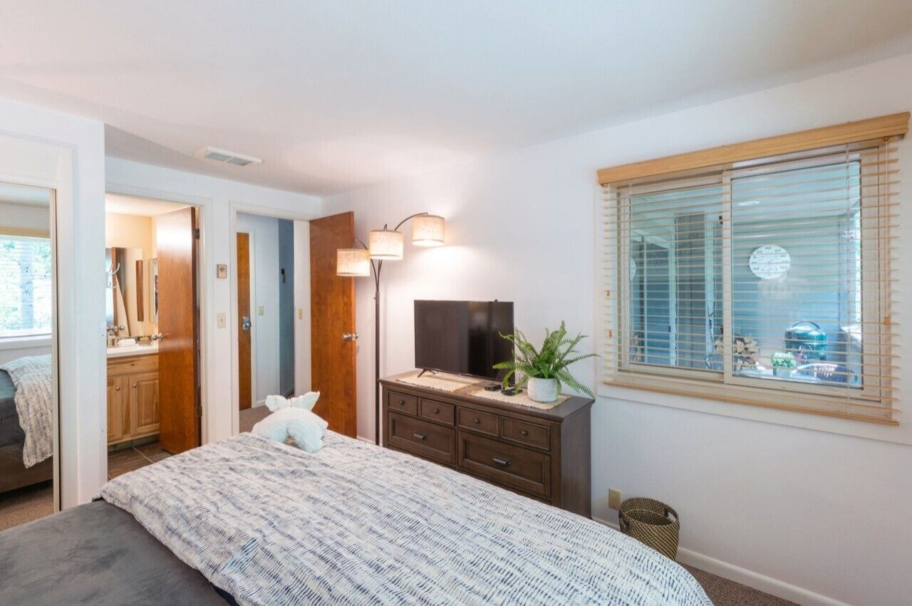 Ein Schlafzimmer mit Bett, Schminktisch, Fernseher und einem Fenster mit Jalousien.