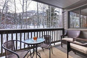 Relax in this serene outdoor space with a view of the snowy landscape, featuring a round table, wicker chairs, and a comfortable sofa.