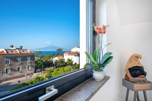 A balcony with a view of the sea and buildings, a potted plant, and a sculpture.