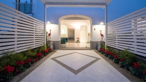 A modern entrance with a geometric tile floor, white slatted walls, and red flowers along the path. - Luxury Apartment with Penthouse and Pool (Sant'Agnello)