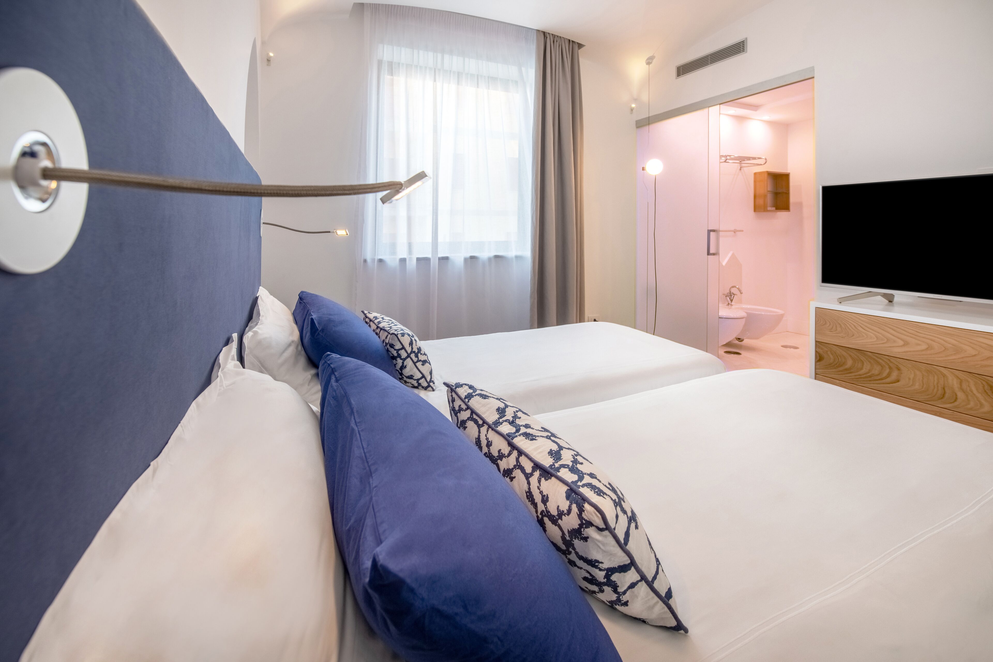 Ett modernt hotellrum med en säng, en tv och ett badrum som syns genom en öppen dörr.