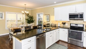A kitchen with white cabinets, stainless steel appliances, a granite countertop, and a dining area with a table and chairs. - Coastal Class Waterfront - "Your Home away from Home" (Rockport)