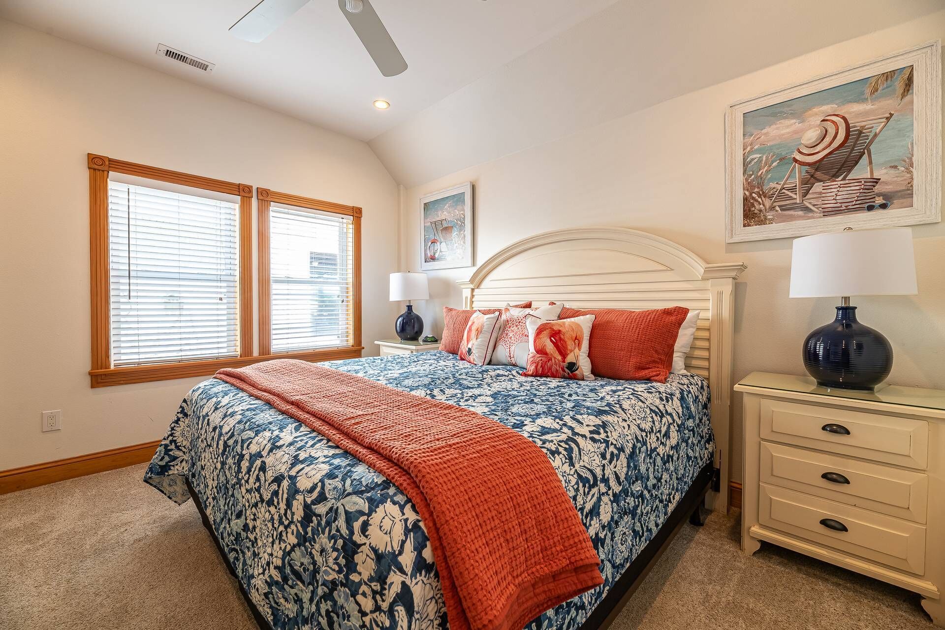 A bedroom with a large bed, two bedside tables, a ceiling fan, and a painting on the wall.