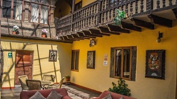 A spacious lobby with two red sofas, a wooden balcony, and a yellow wall adorned with framed pictures. - Cusco Plaza Saphi (Cusco)