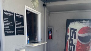 A corner of a building with a white wall, a window, and a door. There are two signs on the wall listing guest policies for a motel. A fire extinguisher is mounted on the wall, and a Pepsi vending machine is visible. - Seaway Motel (Los Angeles)