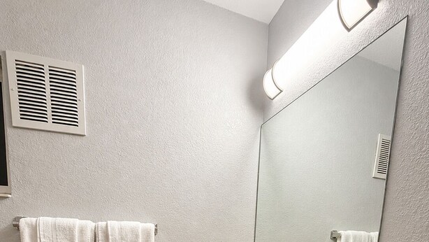 Un baño con un lavamanos color beige, dos toallas blancas, un espejo y un respiradero.