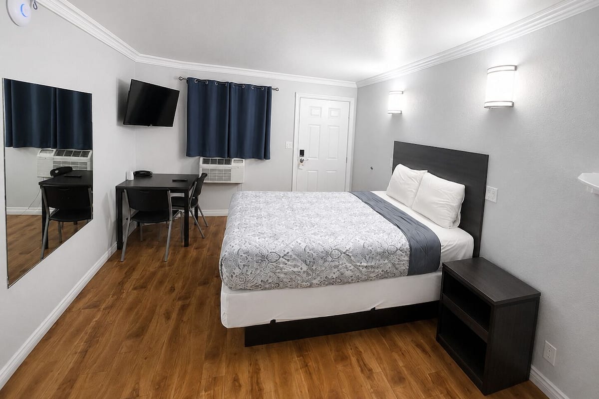 A hotel room with a bed, desk, chair, TV, and a door.