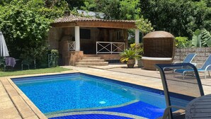 Una piscina con solárium de baldosas, un pequeño pabellón y sillas de descanso.