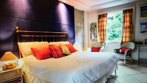 Un dormitorio con una cama grande, una mesita de noche, una silla y una ventana con cortinas.