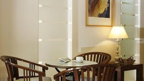 Uma área de jantar com duas cadeiras de madeira, uma mesa redonda, um abajur e uma obra de arte emoldurada na parede.
