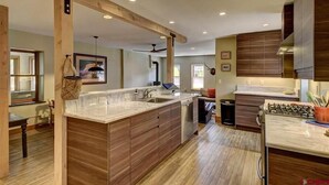 A modern kitchen with wooden cabinetry, a large island with a sink, and a gas stove. - Modern Downtown Loft in Heart of Silverton (Silverton)