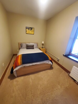 A bedroom with a bed, a nightstand, a lamp, a painting, and a window. - Modern Downtown Loft in Heart of Silverton (Silverton)