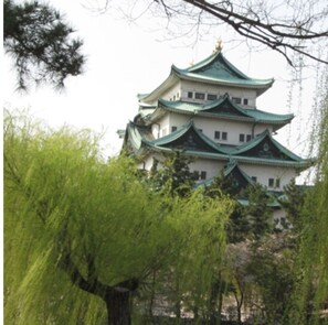 Un château japonais traditionnel, doté de plusieurs niveaux et de toits verts, entouré d’une végétation luxuriante.