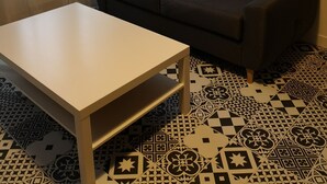 Un salon avec un canapé gris foncé, une table basse blanche, des carreaux de sol à motifs et une décoration murale représentant un cerf.