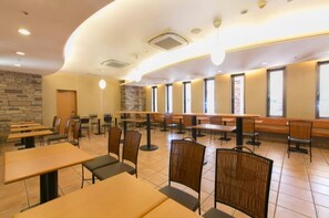 Un amplio comedor interior con varias mesas y sillas, una pared de piedra y ventanas grandes.