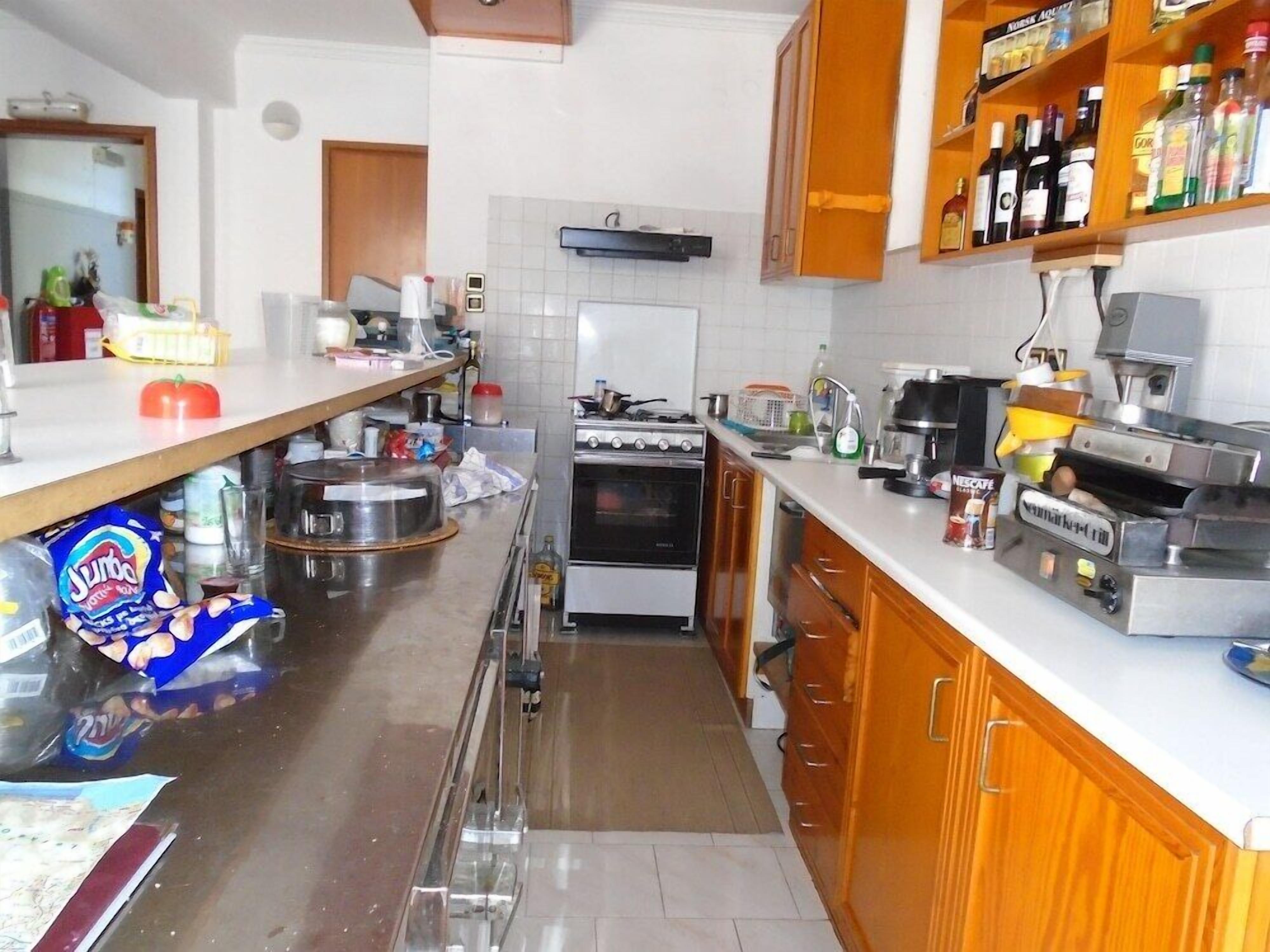 A kitchen with a stove, oven, and various appliances. There is a counter with a coffee maker and a bottle of alcohol. A bag of chips is visible on the counter.