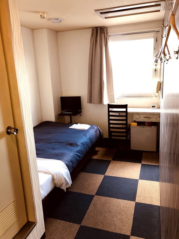 Habitación de hotel pequeña con cama, escritorio, silla, televisor y ventana con cortinas.