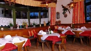 Un restaurant amb diverses taules preparades per dinar, amb camases vermelles i cadires de fusta.