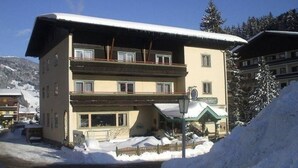 Un hotel de diverses plantes amb un teulat cobert de neu i balcons, envoltat de neu i muntanyes.