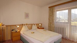 Una habitació d'hotel amb llit, taules de nit, cortines translúcides i vista a l'exterior.