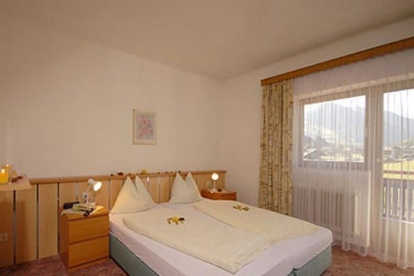 Habitación de hotel con cama, mesitas de noche y vista al exterior, con cortinas translúcidas.