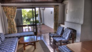 A room with a sofa set, two armchairs, a small table, and a view through a glass door to an outdoor area. - Vilanova Villas (Albufeira)
