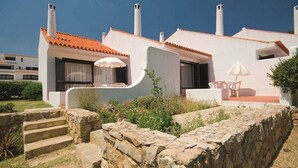 A modern building with a tiled roof, stone steps, and outdoor seating with umbrellas. - Vilanova Villas (Albufeira)