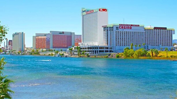 A casino hotel with a prominent casino sign, located near a body of water with clear skies.