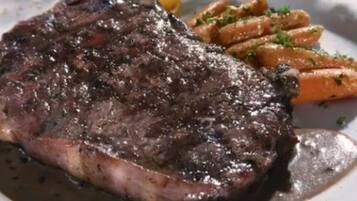 A steak with a dark sauce, accompanied by a side of carrots and a small garnish.