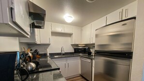 A compact kitchen with white cabinets, a stainless steel refrigerator, a microwave, and a dishwasher.