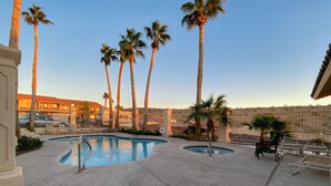 A pool area with multiple pools, palm trees, lounge chairs, and a building in the background.