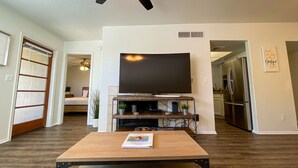 A living room with a flat-screen TV mounted on a wall, a wooden coffee table, and a ceiling fan. - AFFLUENCE ABOUNDS ~ FOOTHILLS CONDO ~ SLEEPS 6 (Tucson)