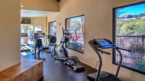 A gym with treadmills, elliptical machines, and exercise bikes, with large windows offering views of the outdoors. - AFFLUENCE ABOUNDS ~ FOOTHILLS CONDO ~ SLEEPS 6 (Tucson)