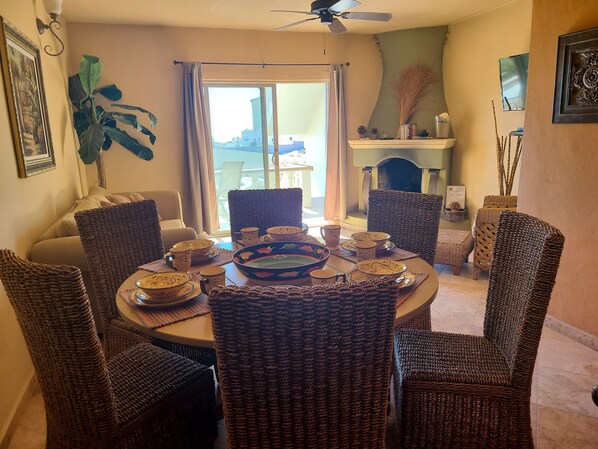 A dining area with wicker chairs and a round table set for a meal, a fireplace, and a view through the glass doors.