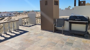 Une terrasse avec un barbecue, une chaise et une vue sur la plage et l’océan.