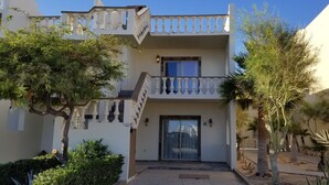Un immeuble de deux étages doté d’un balcon, d’un escalier et d’une entrée fermée par un portail.